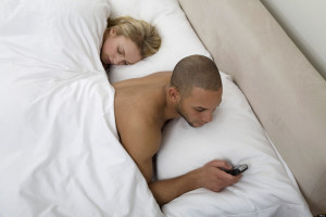 Young man text messaging with young woman sleeping